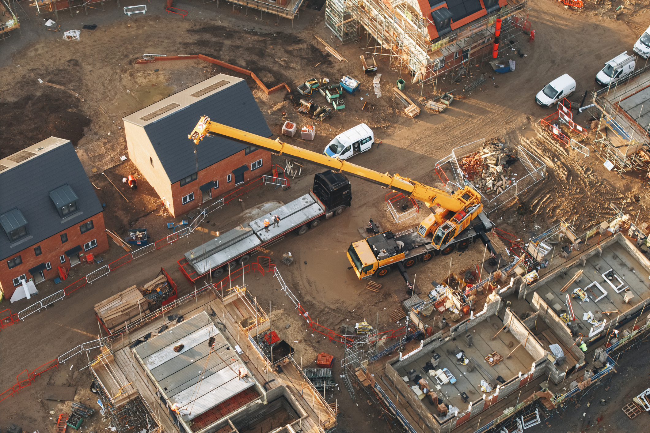 Aerial view of a construction site with houses in various stages of building and a large yellow crane lifting materials.