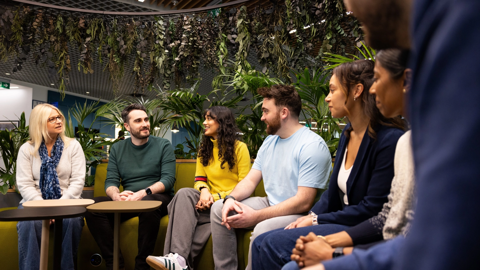 A group of people are seated in a semi-circle on green couches in Legal & General’s Cardiff office. The space is adorned with plants hanging from the ceiling. A group of people are seated in a semi-circle on green couches in Legal & General’s Cardiff office. The space is adorned with plants hanging from the ceiling.
