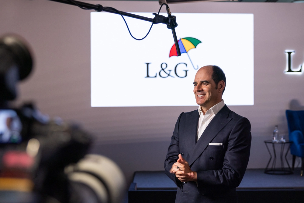 António Simões is standing in front of an empty stage, with the L&G logo projected on the wall. He is wearing a dark suit and white shirt, with his hands clasped in front of him. A microphone boom is positioned above him, and there are cameras and lighting equipment visible in the foreground. António Simões is standing in front of an empty stage, with the L&G logo projected on the wall. He is wearing a dark suit and white shirt, with his hands clasped in front of him. A microphone boom is positioned above him, and there are cameras and lighting equipment visible in the foreground.