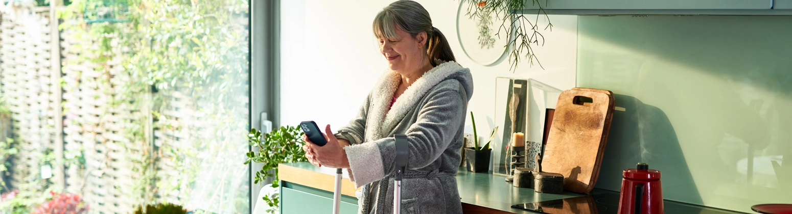 A smiling woman standing in a kitchen focusing on her smart phone. A smiling woman standing in a kitchen focusing on her smart phone.