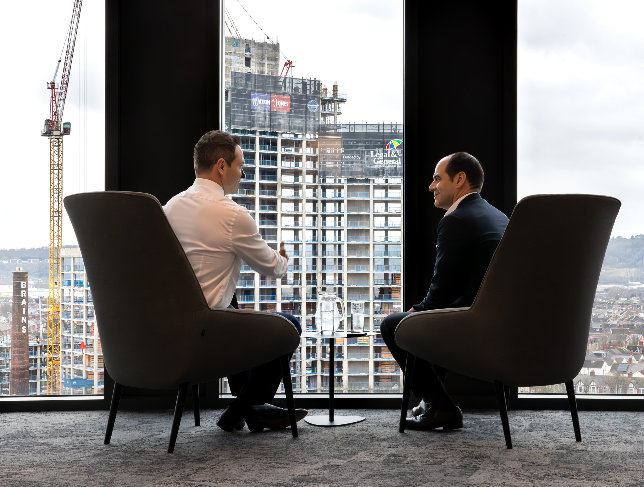António Simões, CEO of Legal & General, seated by a window with a colleague, with construction workers visible outside.