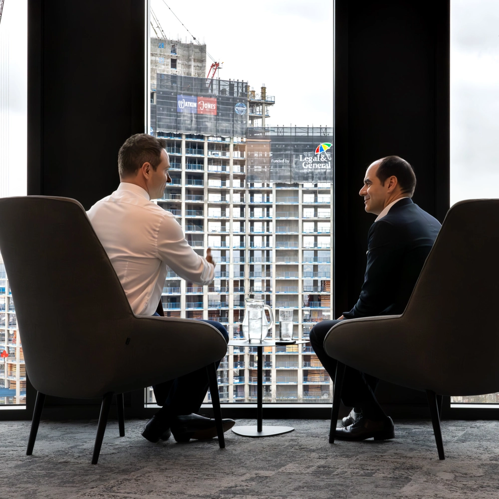 António Simões, CEO of Legal & General, seated by a window with a colleague, with construction workers visible outside. António Simões, CEO of Legal & General, seated by a window with a colleague, with construction workers visible outside.