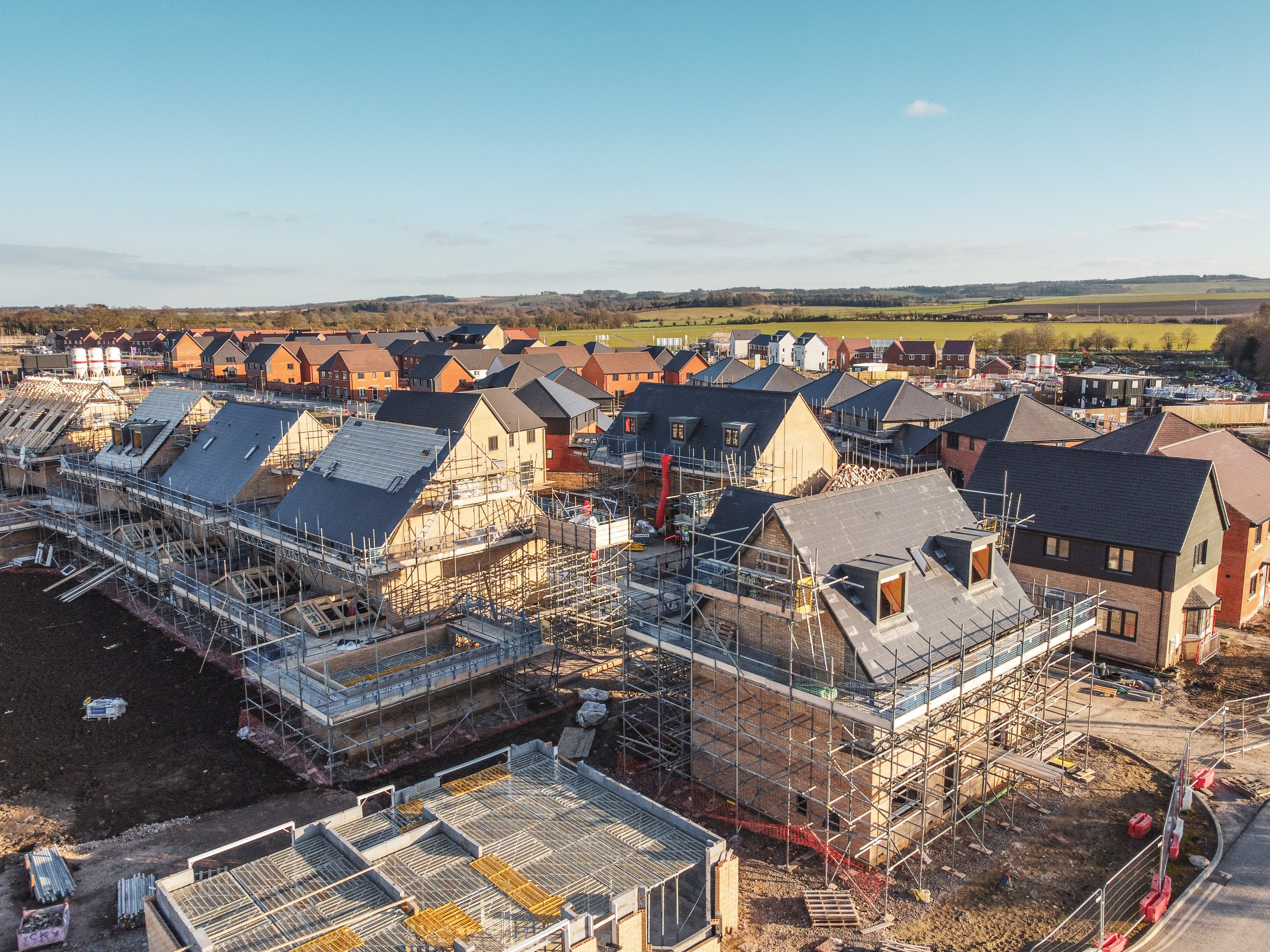 Aerial view of a housing development under construction, with multiple homes in various stages of building and scaffolding visible.