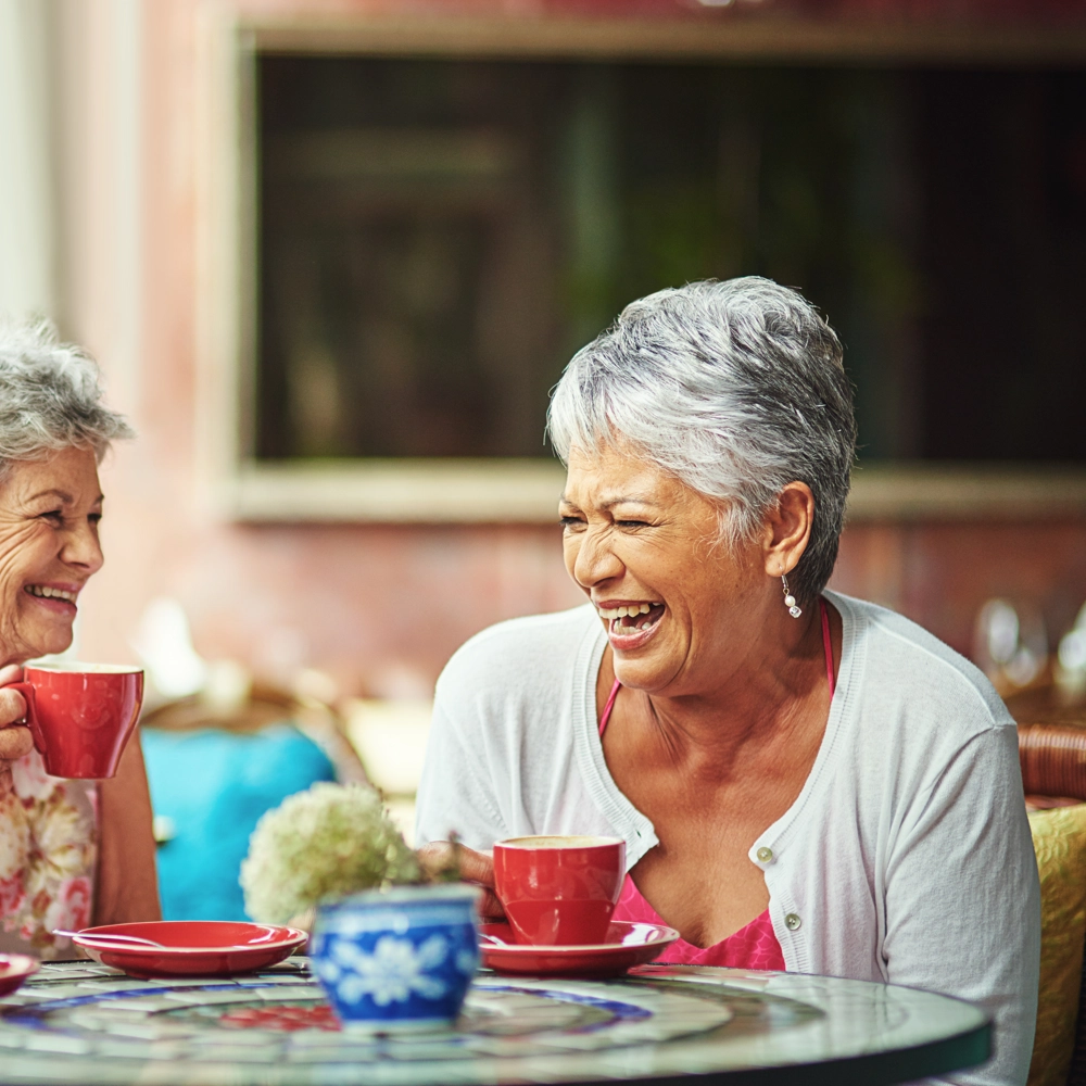 Three adults sitting at a café table, drinking from red cups and talking around a colourful mosaic table. Three adults sitting at a café table, drinking from red cups and talking around a colourful mosaic table.