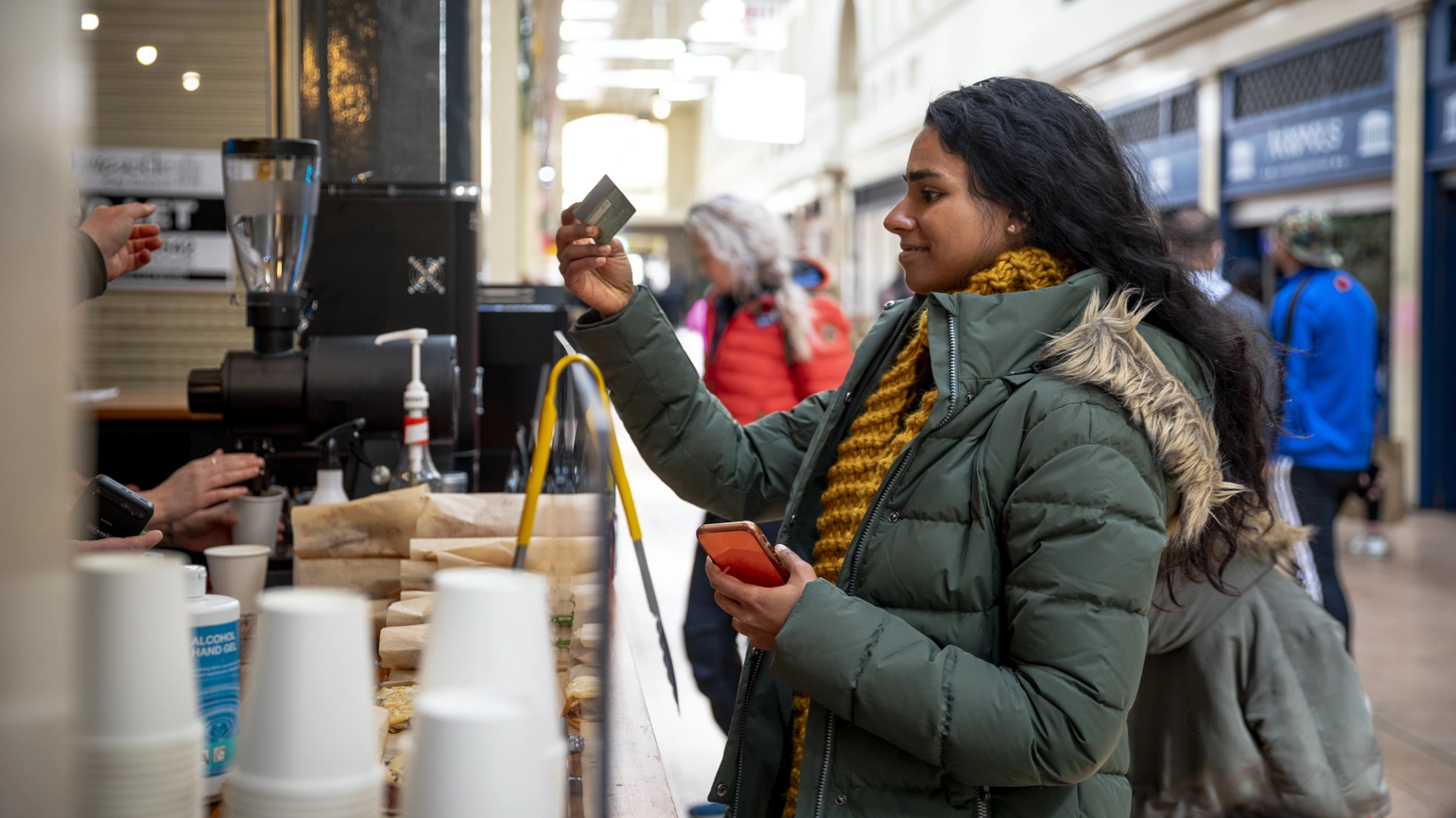 A mid adult woman on a sunny winters day. She is wearing casual, winter clothing and accessories. She is paying for a coffee with her credit card at a small coffee shop in a shopping arcade. A mid adult woman on a sunny winters day. She is wearing casual, winter clothing and accessories. She is paying for a coffee with her credit card at a small coffee shop in a shopping arcade.